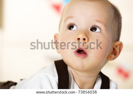 Sweet caucasian baby boy with white shirt and brown suspenders lying on floor and looking up innocently.