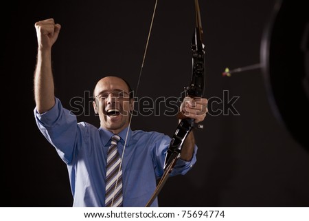 Handsome happy businessman cheering as he hit the target with bow and arrow symbolizing successful business.