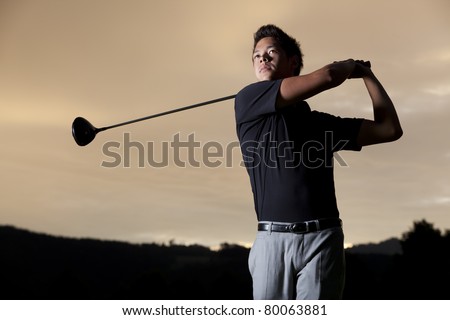 Close up professional golf player in black shirt teeing-off with beautiful sunset in background, front view.