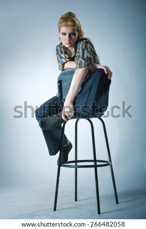Looking young girl in the studio sitting on a bar stool