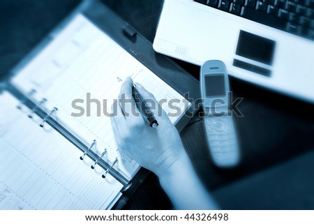 business communications - hand writing in a diary plus laptop and cell phone on a desktop