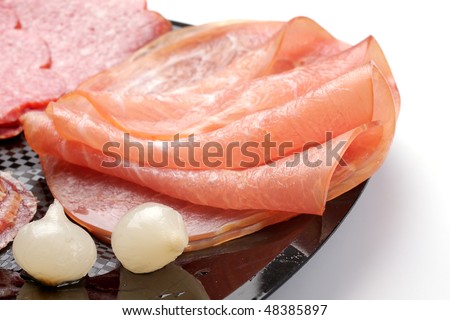 rolled ham, salami and small onions on a black plate
