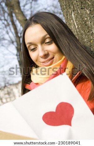 Beautiful female in the park. In the hands of an envelope with a letter. The letter pasted red heart