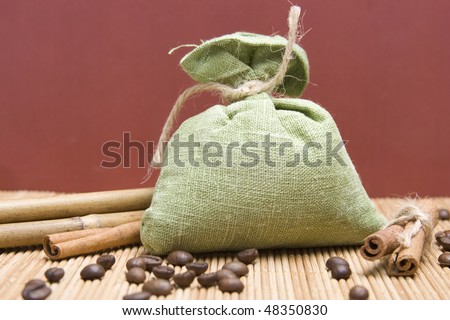 Coffee beans and cinnamon sticks in canvas sack on wooden background. Green bag