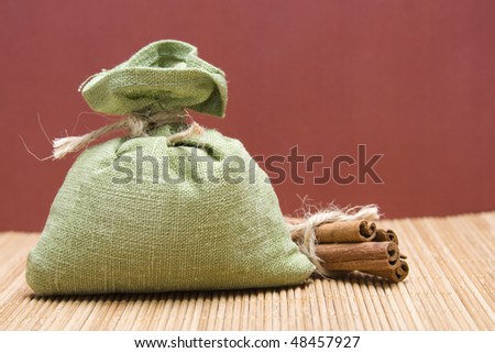 Green bag filled with spices corded near cinnamon sticks