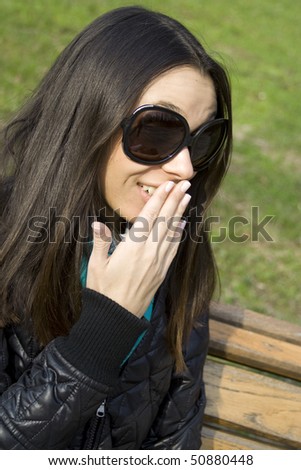 Surprised beautiful woman in the park laughs and covers his mouth with his hand
