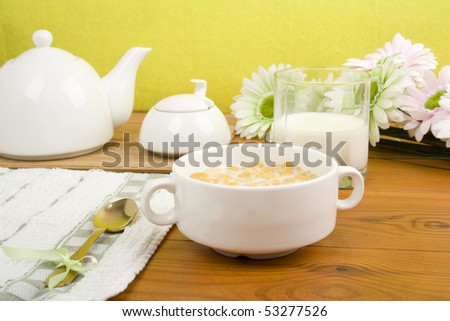 Breakfast. On the wooden table is breakfast cereal with milk, a glass of milk, a spoon, napkin, tea and flowers