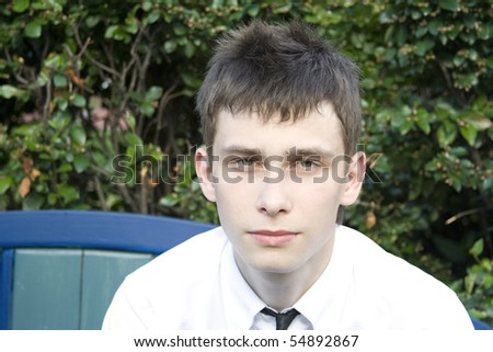 Teenager in a park sitting on a bench in a white shirt and tie look in the frame