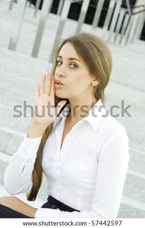 Young business woman on the background of stairs office building whispers trade secrets