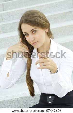 Young businesswoman outdoors on the stairs near the office building shows a sign of 
