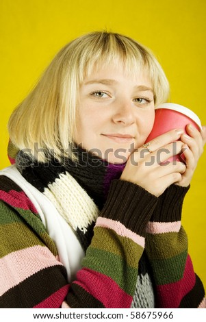 Young woman in sweater and scarf clasps to face a papercup of coffee. Winter