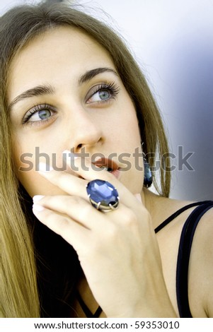 Portrait of elegantly beautiful young woman covers her mouth with his hand. The girl beautiful jewelry, ring and earrings with large blue stones