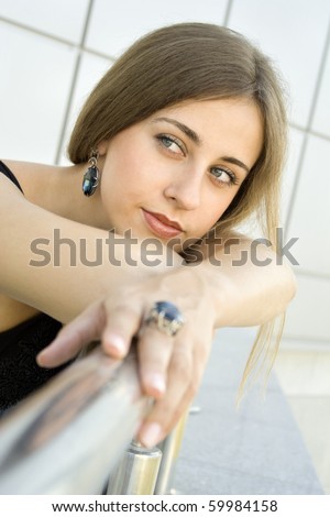 Portrait of elegantly beautiful young woman is based on the railing. The girl beautiful jewelry, ring and earrings with large blue stones