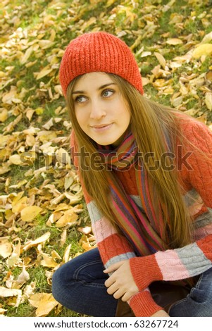 Portrait of a beautiful young woman sitting in a pile of leaves, smiling, looking up