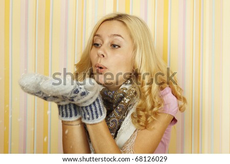 Photos of beautiful young Russian woman in mild winter mittens and a scarf. Blows snowflakes with mittens