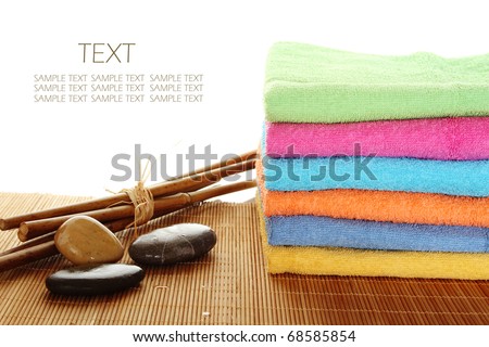 Lots of colorful bath towels stacked on each other. Side by side on a wooden surface lie bamboo sticks and stones. Isolated