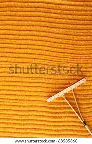 On the golden (orange) sand with wooden rakes made strips. Beside these wooden rakes. Rake in Zen Garden taken closeup
