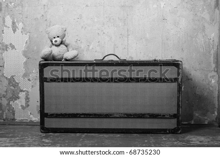 Old-fashioned suitcase standing on the old wooden floor against a shabby walls, suitcases sitting on the edge of Teddy. Forgotten, abandoned
