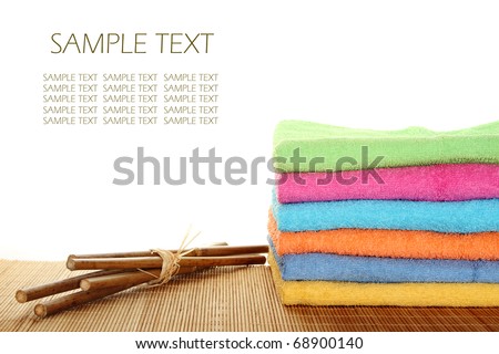 Lots of colorful bath towels stacked on each other. Side by side on a wooden surface lie bamboo sticks. Isolated