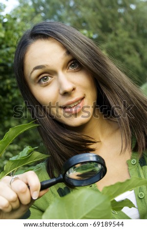 Young woman outdoors looking through a magnifying glass on the green leaves of the tree