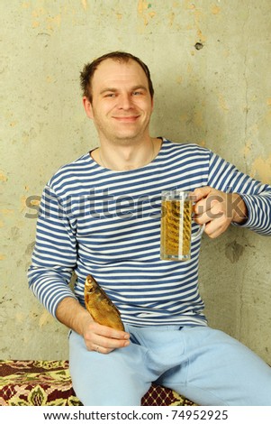 Closeup of a young man with a beer and dried fish. The guy on the background of the old concrete wall in white and blue telnyazhke