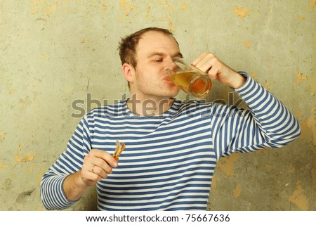 Closeup of a young man with a beer and dried fish. The guy on the background of the old concrete wall in white and blue telnyazhke