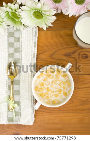 Breakfast. On the wooden table is breakfast cereal with milk, spoon and napkin