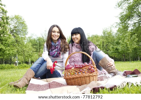 Mother and daughter sitting at a picnic on a blanket next to baskets full of fruit and wine