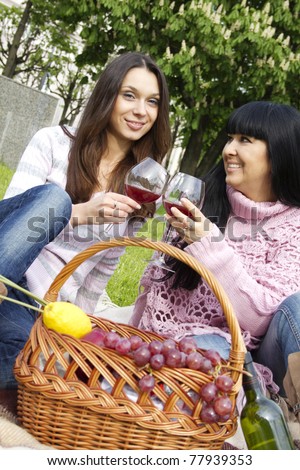 Mother and daughter sitting at a picnic on a blanket drinking wine next to a fruit basket