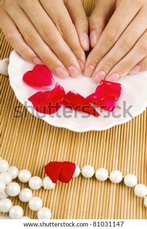 Close-up of beautiful girls hands in the water next to the rose petals