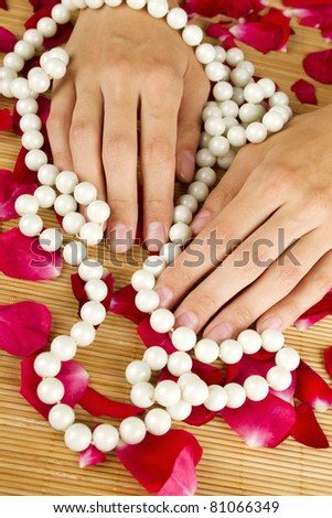 Close-up of beautiful hand braided with pearls and lie on red rose petals
