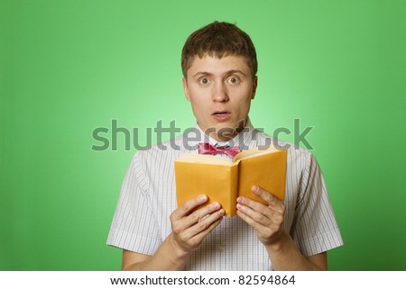 Young attractive man in a shirt and bow tie on a green background reads the yellow book. Bookworm