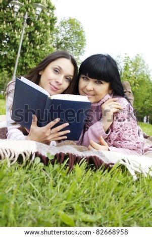 Attractive Mom and daughter, a teenager in a park reading a book and make merry