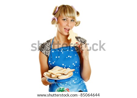 Pretty young woman in an apron and oven gloves holding a plate of gingerbread cookies for the little people christmas. Tries to bite one cookie