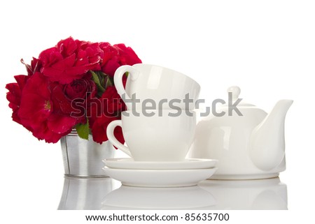 White crockery for tea kettle, two cups and saucers and a bouquet of red roses in a small iron bucket