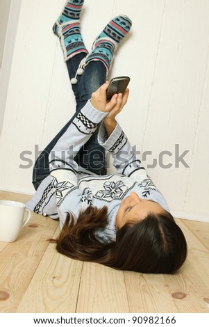 Young woman lying at home on the floor, legs raised up and lean on the wall with a mobile phone