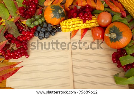 The frame of the gifts of autumn pumpkins, corn, fall leaves, tomatoes, red berry cranberry and grapes are in the old printed music sheets