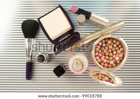 Cosmetics on the table. Basic colors pink and gold. Powder, skin cream, lipstick, handbag, vanity case, brush, eyeliner