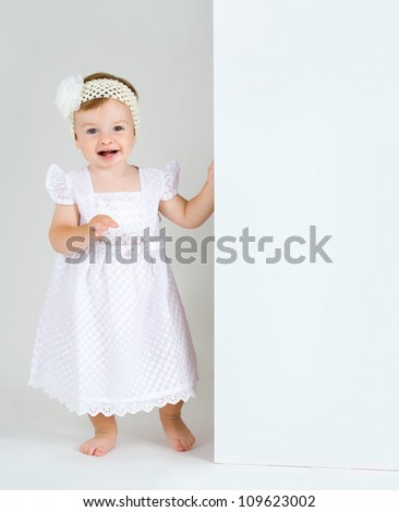 Studio Isolation of an Infant Child. The baby girl is Isolated on white with a Horizontal composition. She is holding a white board with copy space for text and has a huge surprised smiling expression