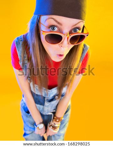 Portrait of funny girl in glasses and a brown hat. Stares at the viewer. Isolation on a yellow background.