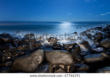 coast with rocks in foreground and moonlight reflecting off water at night