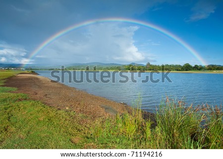 morning rainbow on cloudy sky with lake in foreground (upper coomera,qld,australia)
