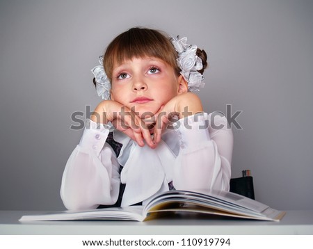 The beautiful girl with books sits at a school table fnd dreams