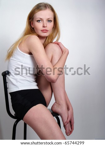 The beautiful weakened girl with long feet sits on a chair