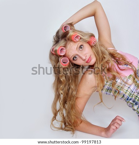 The beautiful happy girl with long light hair twists big hair curlers