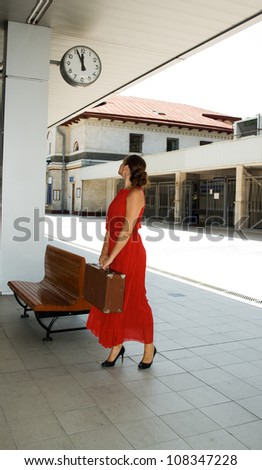 woman with a suitcase looks at the clock while standing on the platform