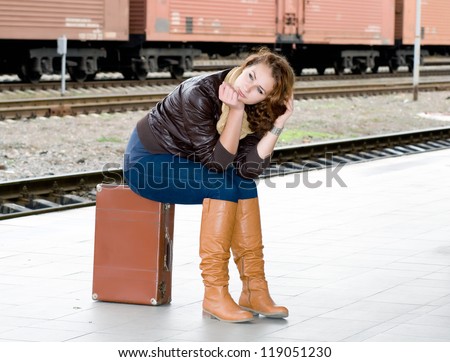 girl is sitting on a suitcase waiting for the train