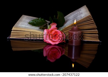 Open book, Rose and a burning candle on a black background