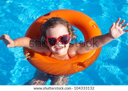 Funny little girl swims in a pool in an orange life preserver