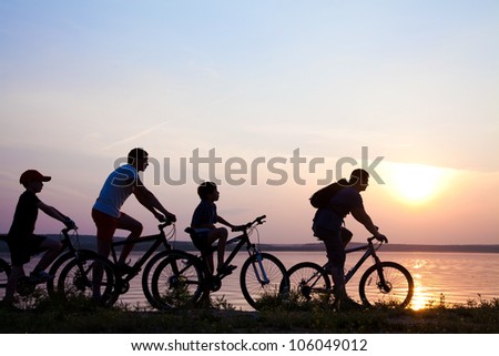 family on bicycles admiring the sunset on the lake. silhouette